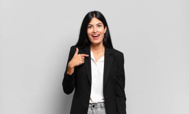 Genç İspanyol iş kadını mutlu, gururlu ve şaşırmış görünüyor, neşeli bir şekilde kendini gösteriyor, kendinden emin ve yüce hissediyor.