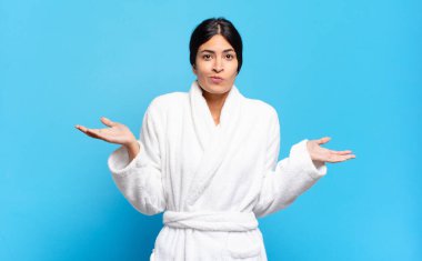 Genç İspanyol kadın şaşkın ve şaşkın hissediyor, şüpheci, farklı seçenekleri tartıyor ya da komik bir ifadeyle seçiyor. Bornoz konsepti