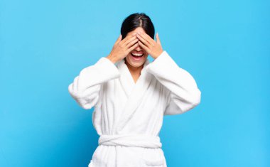 Genç İspanyol kadın gülümsüyor ve mutlu hissediyor, iki eliyle gözlerini kapatıyor ve inanılmaz bir sürpriz bekliyor. Bornoz konsepti