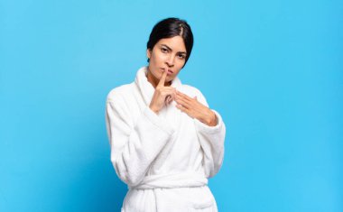 Genç İspanyol kadın ciddi görünüyor ve parmaklarını dudaklarına bastırıp sessizlik ya da sessizlik talep ediyor, sır saklıyor. Bornoz konsepti