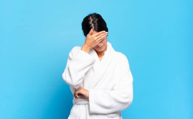 Genç İspanyol kadın stresli, utanmış ya da üzgün görünüyor, baş ağrısı var, yüzünü eliyle kapatıyor. Bornoz konsepti