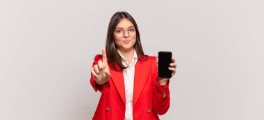 Genç iş kadını gururla gülümsüyor ve gururla bir numaralı pozunu veriyor, kendini lider gibi hissediyor.