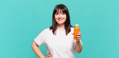 Mutlu bir şekilde gülümsüyor, eli kalçasında ve kendinden emin, olumlu, gururlu ve arkadaş canlısı bir tavırla.