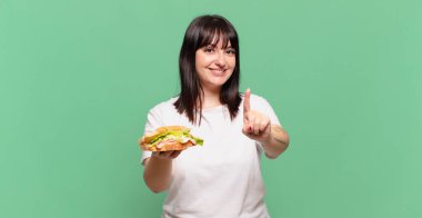 Gururla ve kendinden emin bir şekilde gülümseyerek bir numaralı pozu vererek, bir lider gibi hissederek.