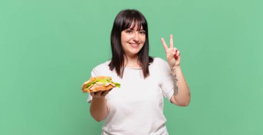 Gülümsüyor ve dost canlısı görünüyor. İki ya da iki numarayı gösteriyor. Elini ileri uzatıp geri sayıyor.