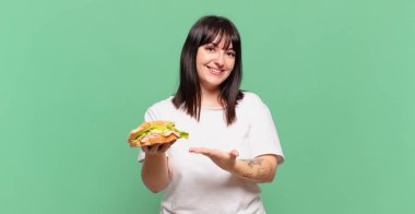 Neşeli bir şekilde gülümsüyor, mutlu hissediyor ve bir konsepti fotokopi uzayında avuç içiyle gösteriyor.