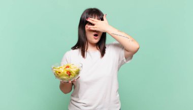 Şok olmuş, korkmuş ya da korkmuş görünüyor, yüzleri elle kaplıyor ve parmaklarının arasına bakıyor.