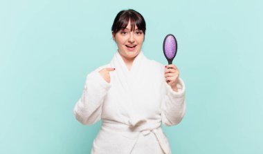 Bornoz giyen genç bir kadın mutlu, şaşkın ve gururlu, heyecanlı, şaşkın bakışlarla kendini işaret ediyor.