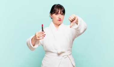 Bornoz giyen genç bir kadın kızgın, sinirli, hayal kırıklığına uğramış ya da hoşnutsuz, ciddi bir bakışla başparmağını kaldırıyor.