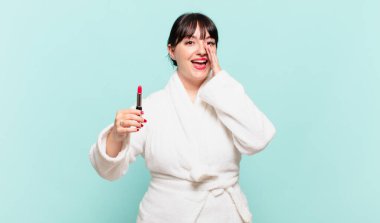 Bornoz giymiş genç bir kadın mutlu, heyecanlı ve pozitif hissediyor. Elleri ağızda, bağırıyor.