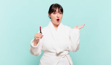 Bornoz giymiş genç bir kadın şaşırmış ve şoka uğramış görünüyor. Çenesi düşmüş ve eli açık bir objeyi tutuyor.