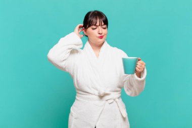 Bornoz giymiş genç bir kadın şaşkın ve şaşkın hissediyor, başını kaşıyor ve yan tarafa bakıyor.