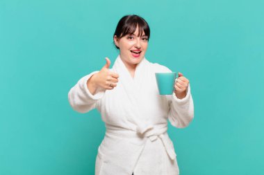 Bornoz giyen genç bir kadın gururlu, tasasız, kendinden emin ve mutlu, başparmağıyla gülümsüyor.