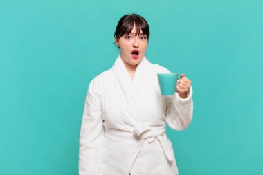 Bornoz giymiş genç bir kadın şok olmuş ya da şaşırmış görünüyor, ağzı açık bir şekilde 