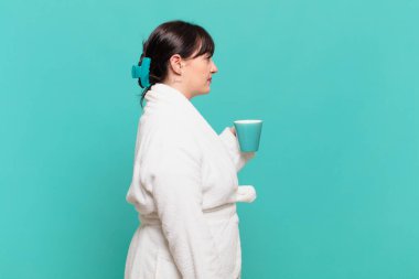 Profil görüntüsünde bornoz giyen genç bir kadın ilerideki boşluğu kopyalamak istiyor, düşünüyor, hayal ediyor ya da hayal kuruyor.