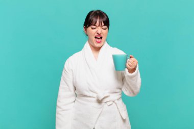 Bornoz giymiş genç bir kadın agresif bir şekilde bağırıyor, çok kızgın, sinirli, öfkeli ya da sinirli görünüyor.