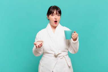 Bornoz giymiş genç bir kadın ağzı açık ve şaşırmış, şok olmuş ve hayrete düşmüş.