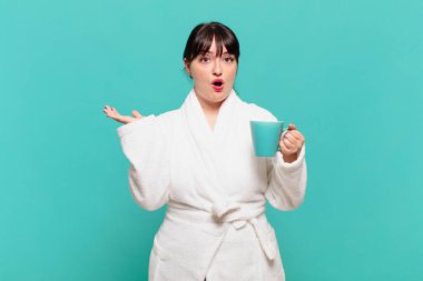 Bornoz giymiş genç bir kadın şaşırmış ve şoka uğramış görünüyor. Çenesi düşmüş ve eli açık bir objeyi tutuyor.