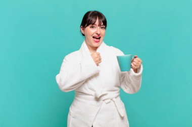 Bornoz giyen genç bir kadın mutlu, pozitif ve başarılı hissediyor, bir meydan okumayla karşılaştığında motive oluyor veya iyi sonuçları kutluyor.