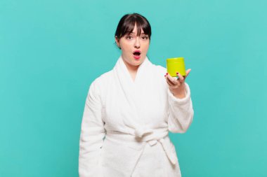 Bornoz giymiş genç bir kadın şok olmuş ya da şaşırmış görünüyor, ağzı açık bir şekilde 