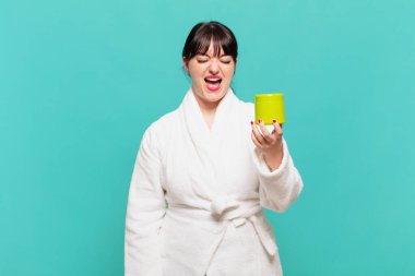 Bornoz giymiş genç bir kadın agresif bir şekilde bağırıyor, çok kızgın, sinirli, öfkeli ya da sinirli görünüyor.