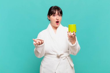 Bornoz giymiş genç bir kadın ağzı açık ve şaşırmış, şok olmuş ve hayrete düşmüş.