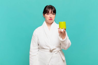 Bornoz giyen genç bir kadın üzgün ve mızmız, mutsuz bir bakışla, olumsuz ve hayal kırıklığına uğramış bir tavırla ağlıyor.