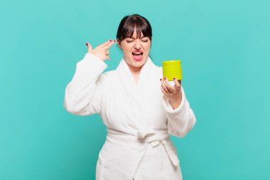 Bornoz giymiş genç bir kadın mutsuz ve stresli görünüyor, intihar jesti elle silah işareti yapıyor, kafasını işaret ediyor.