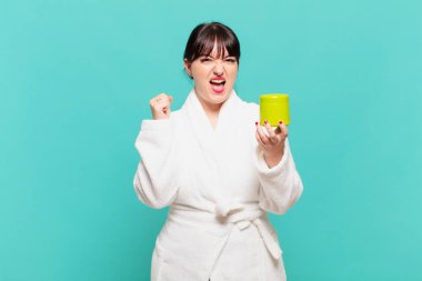 Bornoz giymiş genç bir kadın kızgın bir ifadeyle agresif bir şekilde bağırıyor ya da yumruklarıyla başarıyı kutluyor.