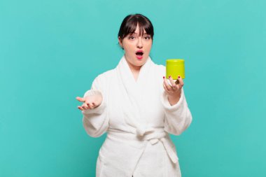 Bornoz giymiş genç bir kadın şok olmuş, şaşırmış, endişeli ve paniklemiş, stresli ve dehşete kapılmış görünüyor.