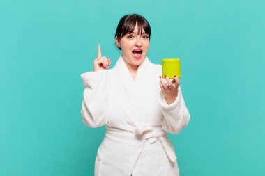 Bornoz giyen genç bir kadın bir fikri fark ettikten sonra mutlu ve heyecanlı bir dahi gibi hissediyor. Neşeli bir şekilde parmak kaldırıyor.!