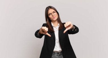 Genç iş kadını üzgün, hayal kırıklığına uğramış ya da kızgın görünüyor. Anlaşmazlıkta baş parmağını gösteriyor. Hayal kırıklığına uğramış hissediyor.