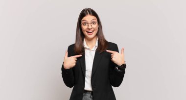 Genç iş kadını mutlu, şaşkın ve gururlu hissediyor. Heyecanlı ve şaşkın bir bakışla kendini işaret ediyor.