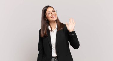 Genç iş kadını mutlu ve neşeyle gülümsüyor, el sallıyor, seni selamlıyor ve selamlıyor, ya da hoşça kal diyor.