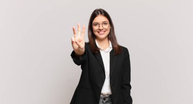 Genç iş kadını gülümsüyor ve arkadaş canlısı görünüyor, üç ya da üç numarayı gösteriyor, elleri önde, geriye doğru sayıyor.