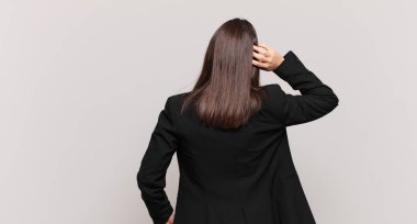 Genç iş kadını düşünüyor ya da şüphe ediyor, kafasını kaşıyor, kafası karışık ve kafası karışık hissediyor, arkaya ya da arkaya bakıyor.