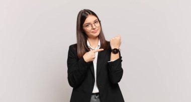 Genç iş kadını sabırsız ve kızgın görünüyor, saati gösteriyor, dakiklik istiyor, zamanında gelmek istiyor.