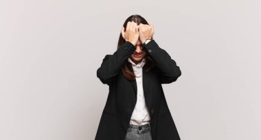 Genç iş kadını stresli ve endişeli, depresif ve hayal kırıklığına uğramış hissediyor, iki elini de başa kaldırıyor.