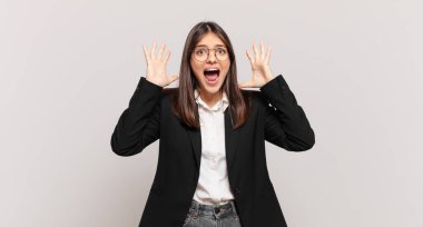 Genç iş kadını panik ya da öfke içinde bağırıyor, şok olmuş, korkmuş ya da öfkeli, elleri başının yanında.