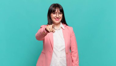 Genç iş kadını kameraya tatmin olmuş, kendinden emin, dostane bir gülümsemeyle bakıyor ve seni seçiyor.