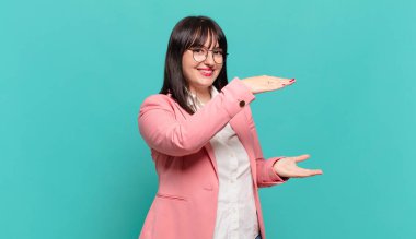 Genç iş kadını gülümsüyor, mutlu, pozitif ve tatmin olmuş hissediyor, fotokopi alanında nesne ya da konsept tutuyor ya da gösteriyor