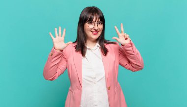 Genç iş kadını gülümsüyor ve arkadaş canlısı görünüyor, 8 ya da 8 numarayı gösteriyor, elleri önde, geri sayıyor.