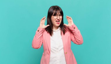 Genç iş kadını panik ya da öfke içinde bağırıyor, şok olmuş, korkmuş ya da öfkeli, elleri başının yanında.