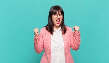 Genç iş kadını öfkeli bir ifadeyle ya da yumruklarıyla başarıyı kutlarken agresif bir şekilde bağırıyor.