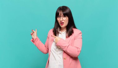 Genç iş kadını şaşkın ve şaşırmış hissediyor. Kenardaki fotokopi alanını işaret ediyor. Şaşırmış, ağzı açık bir bakış.