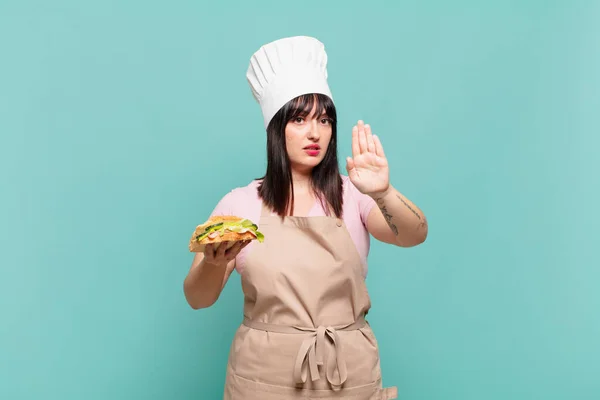 young chef woman looking serious, stern, displeased and angry showing open palm making stop gesture