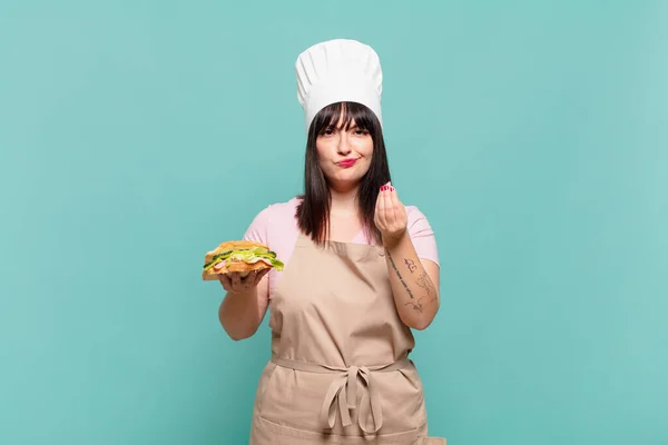 young chef woman making capice or money gesture, telling you to pay your debts!