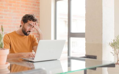 Evde dizüstü bilgisayarla çalışan sakallı genç bir adam.