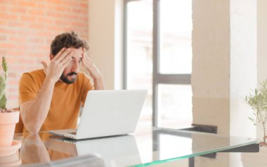 Evde dizüstü bilgisayarla çalışan sakallı genç bir adam.