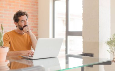 Evde dizüstü bilgisayarla çalışan sakallı genç bir adam.